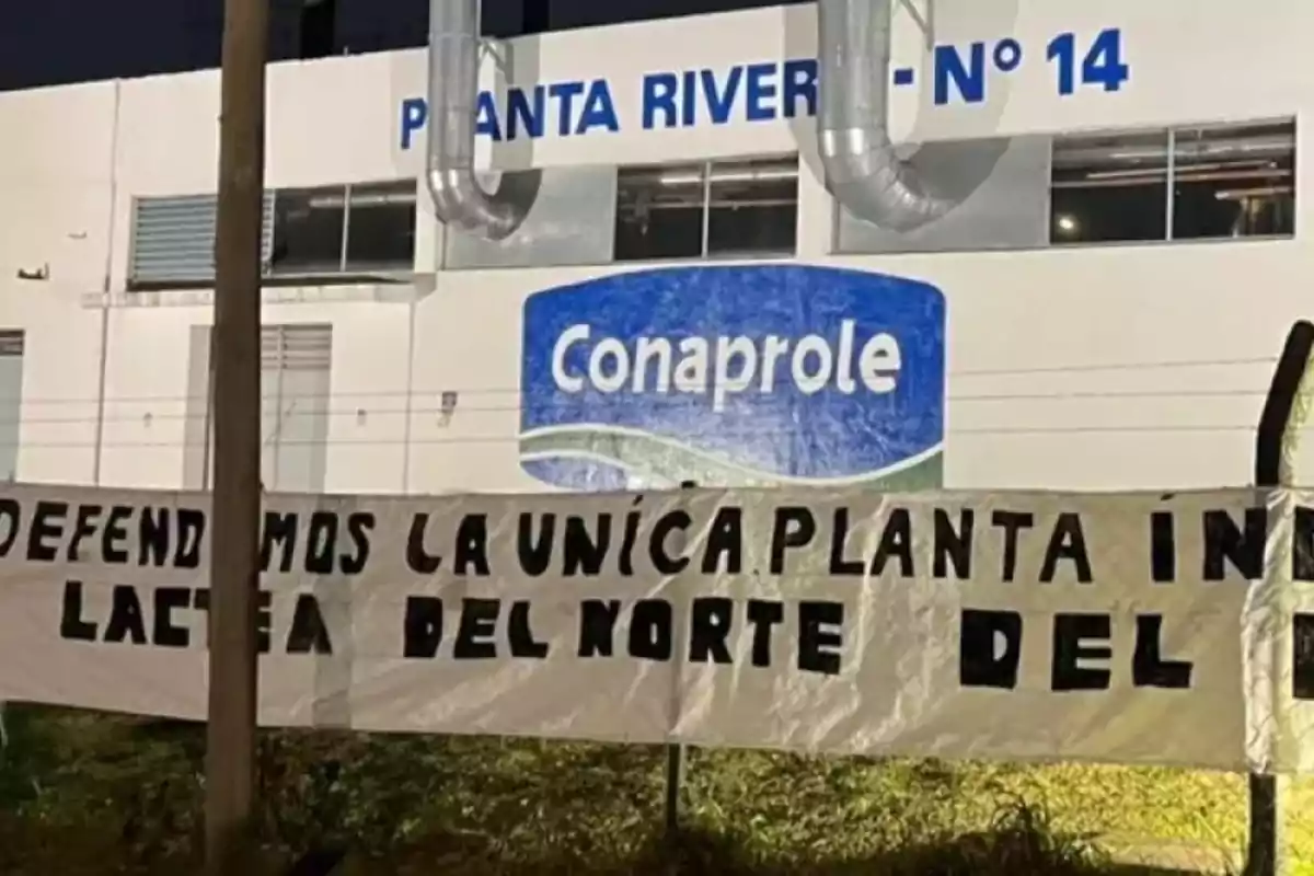 Fachada de una planta industrial de Conaprole con un cartel que dice defendemos la única planta láctea del norte