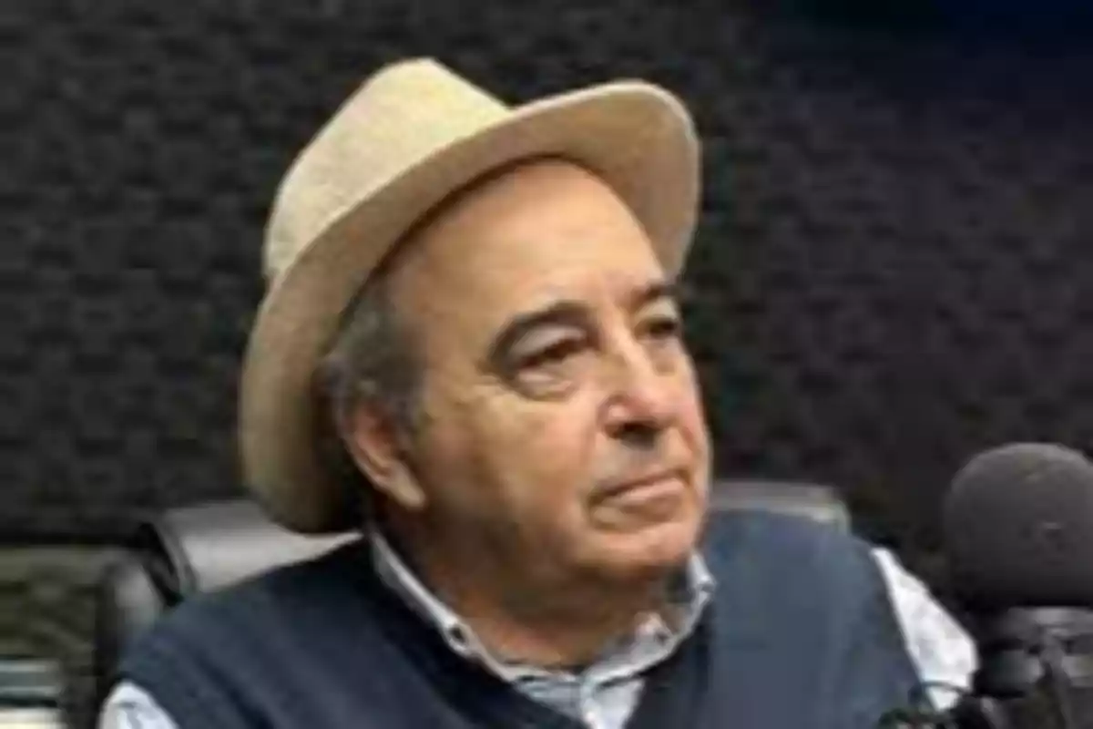 Older man with a light-colored hat sitting in front of a microphone in a recording studio