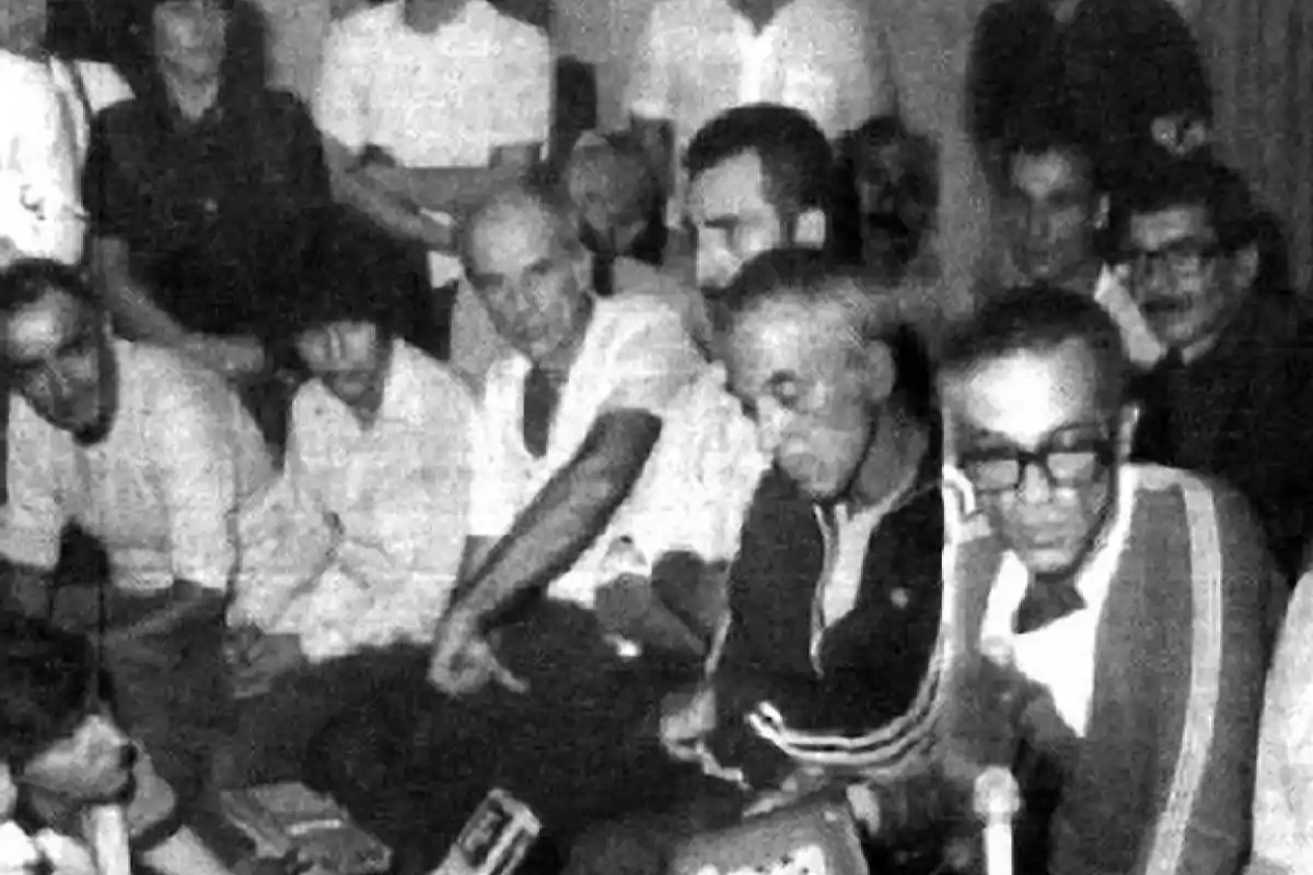 Grupo de personas reunidas en una habitación, algunas sentadas y otras de pie, en una imagen en blanco y negro de aspecto antiguo Grupo de personas reunidas en una habitación, algunas sentadas y otras de pie, en una imagen en blanco y negro de aspecto antiguo