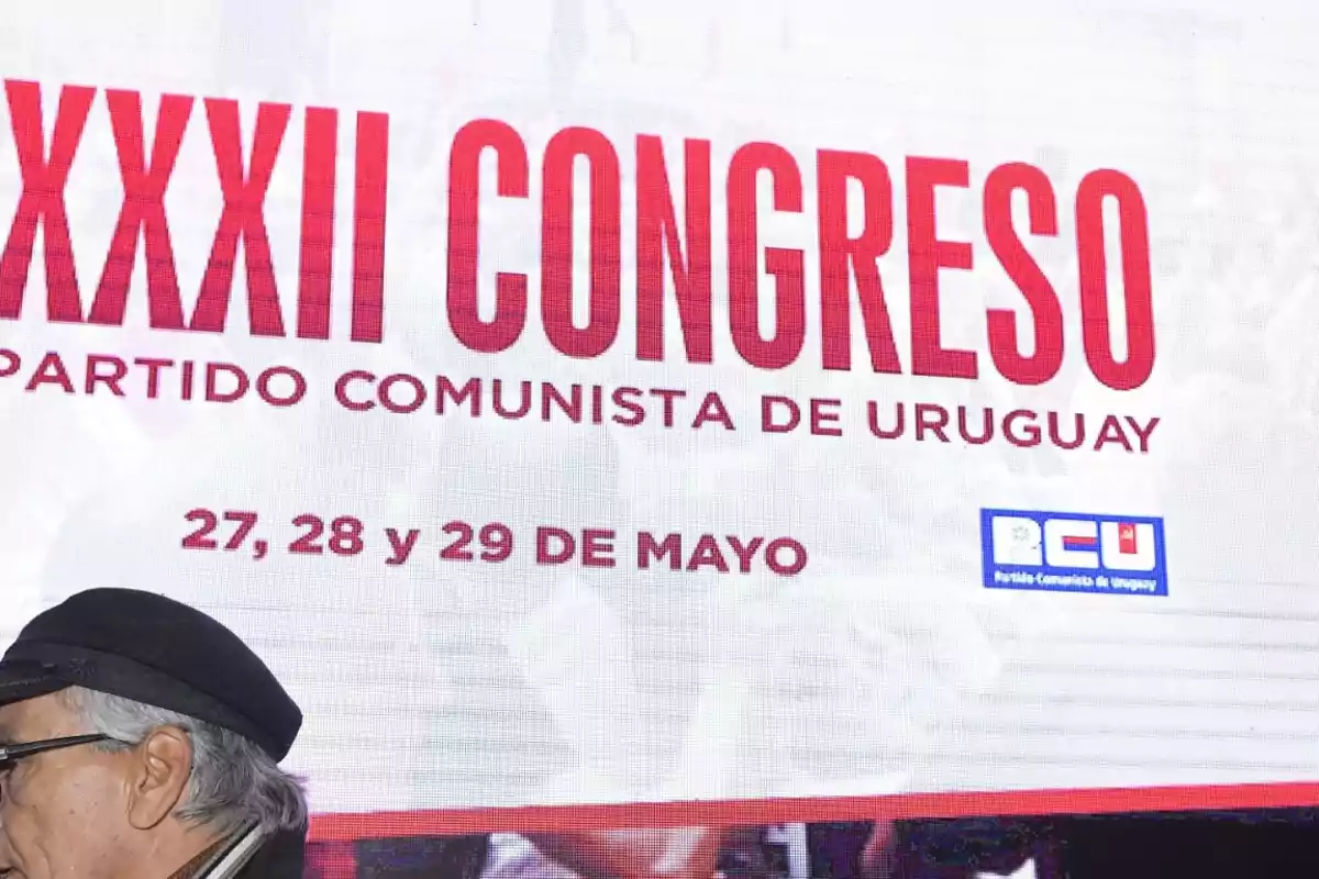 Hombre mayor con boina frente a una pantalla que anuncia el XXXII Congreso del Partido Comunista de Uruguay los días 27, 28 y 29 de mayo Hombre mayor con boina frente a una pantalla que anuncia el XXXII Congreso del Partido Comunista de Uruguay los días 27, 28 y 29 de mayo