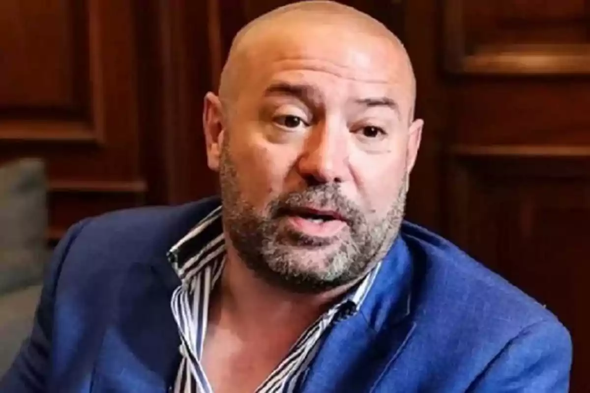 Bald man with a beard and a blue jacket sitting in an indoor setting with wooden walls Bald man with a beard and a blue jacket sitting in an indoor setting with wooden walls