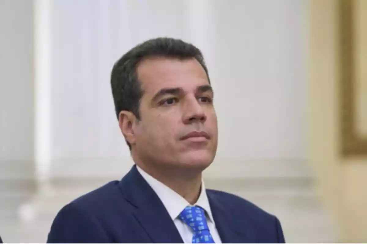 Hombre de cabello corto y oscuro vistiendo traje azul y corbata azul con fondo claro y desenfocado Hombre de cabello corto y oscuro vistiendo traje azul y corbata azul con fondo claro y desenfocado