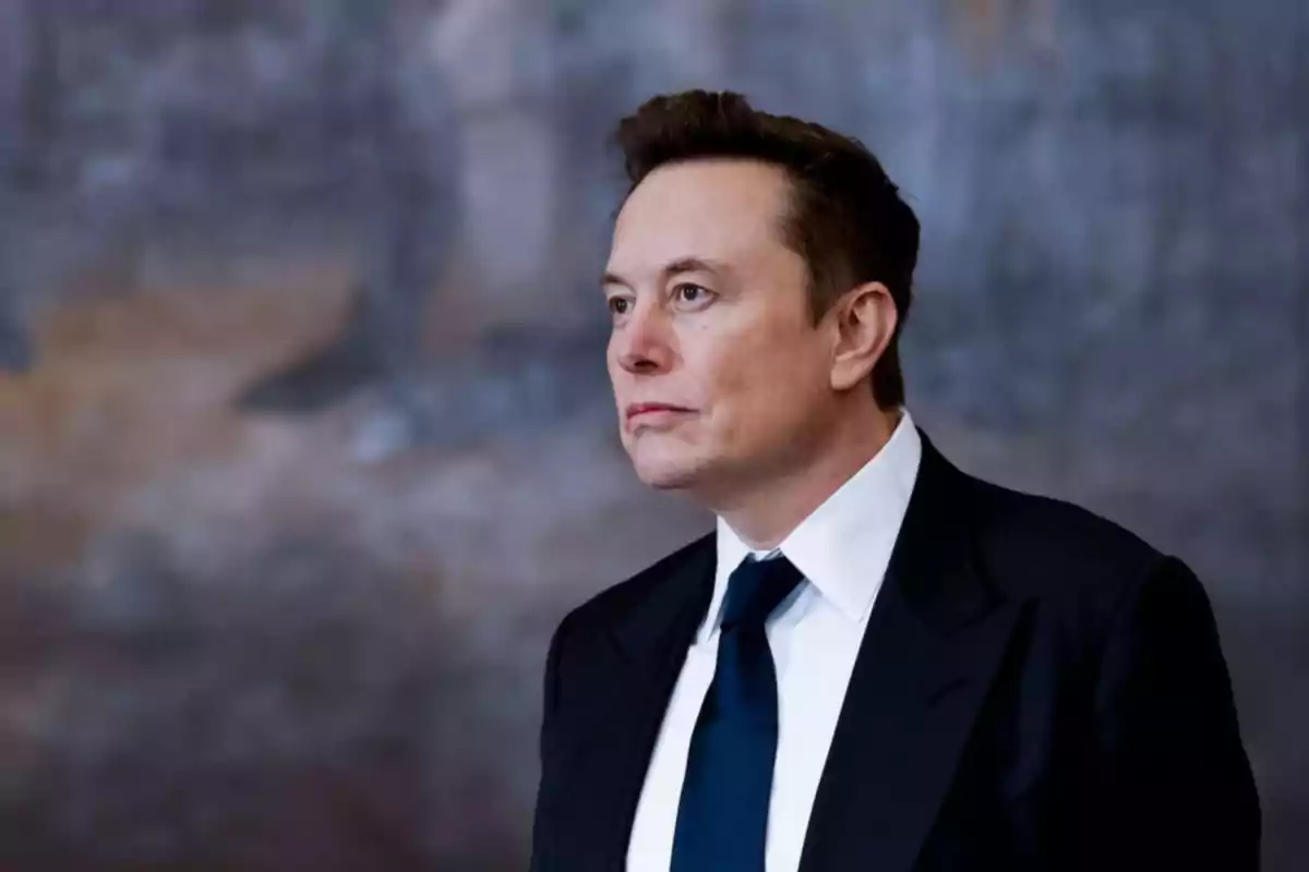 Short brown-haired man in a dark suit and blue tie looking to the right against a blurred background. Short brown-haired man in a dark suit and blue tie looking to the right against a blurred background.