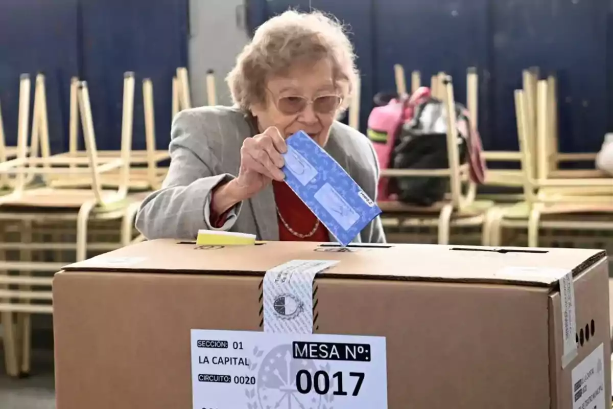 Elderly woman casting her vote in a ballot box during an election day in a classroom with stacked chairs in the background Elderly woman casting her vote in a ballot box during an election day in a classroom with stacked chairs in the background