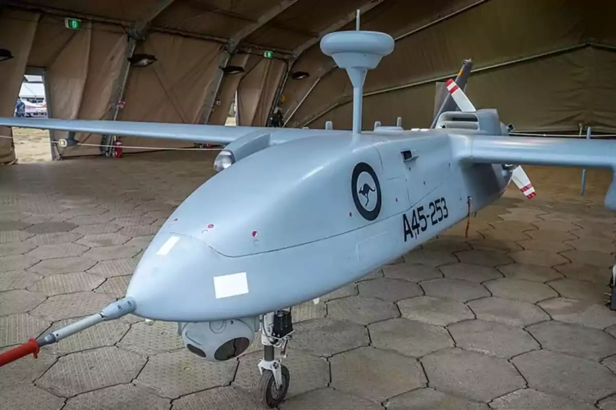 Dron militar gris estacionado dentro de un hangar con piso de loseta hexagonal