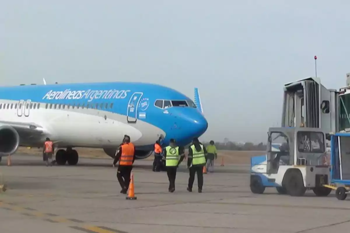 Avión de Aerolíneas Argentinas en pista con personal de seguridad y equipaje trabajando alrededor