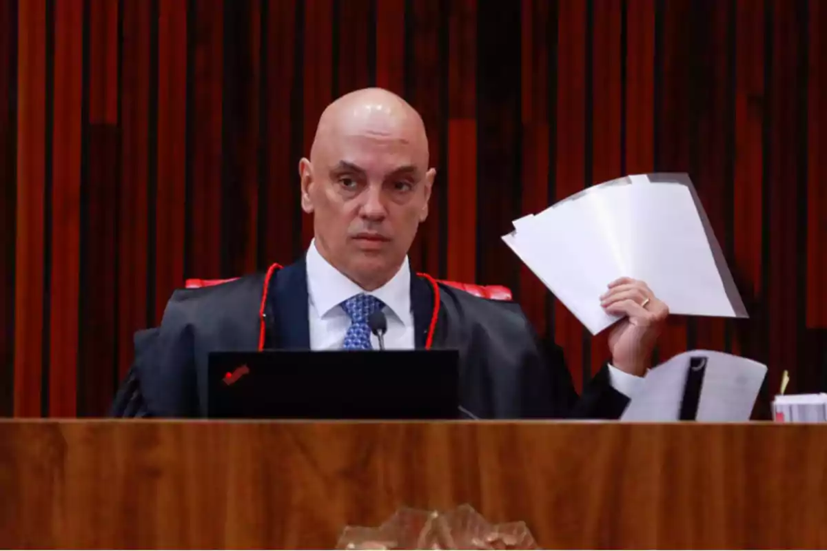 Judge seated on a bench holding several documents in his right hand with a serious expression Judge seated on a bench holding several documents in his right hand with a serious expression