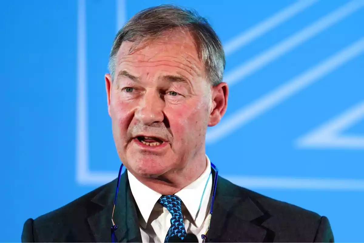 Middle-aged man in a suit and blue tie speaking in front of a blue background Middle-aged man in a suit and blue tie speaking in front of a blue background
