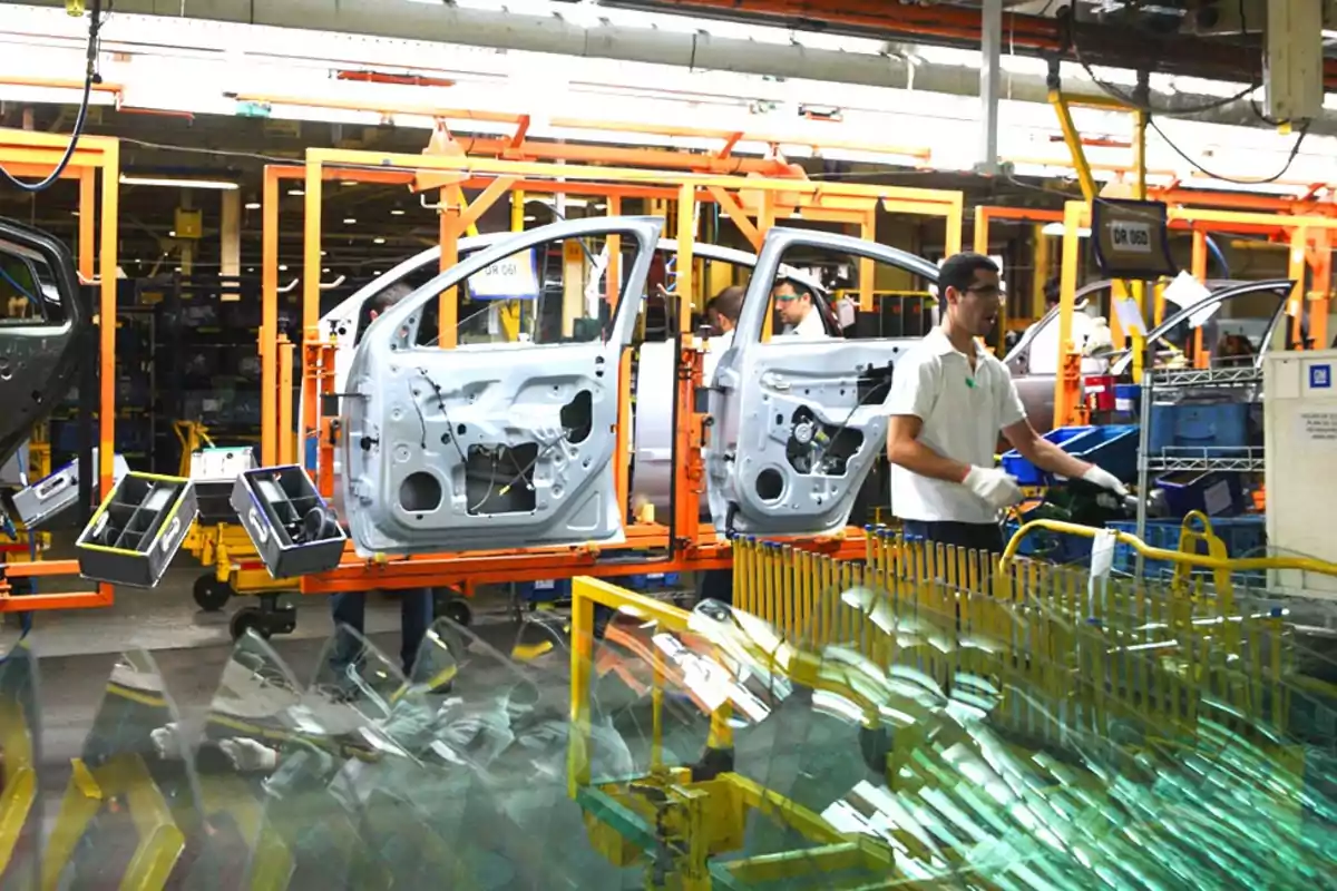 Trabajador ensamblando puertas de automóvil en una línea de producción industrial rodeado de herramientas y piezas de vidrio. Trabajador ensamblando puertas de automóvil en una línea de producción industrial rodeado de herramientas y piezas de vidrio.