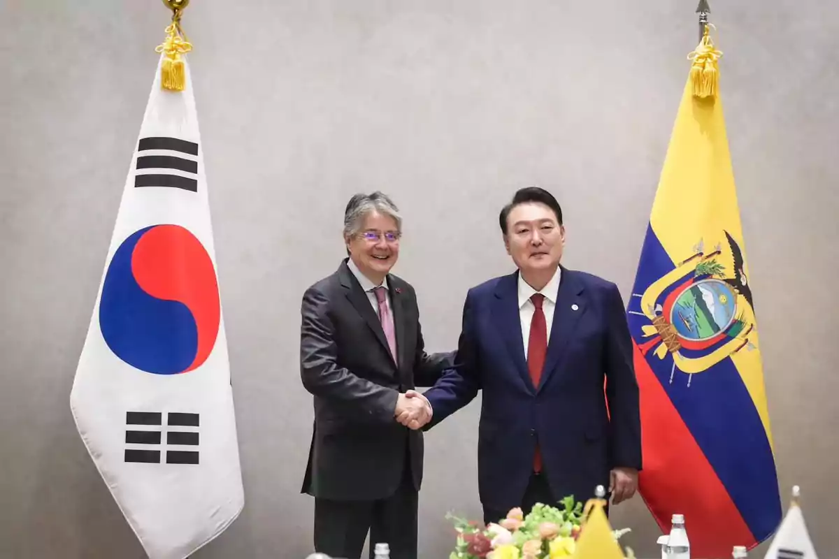 Dos hombres de traje se dan la mano frente a las banderas de Corea del Sur y Ecuador
