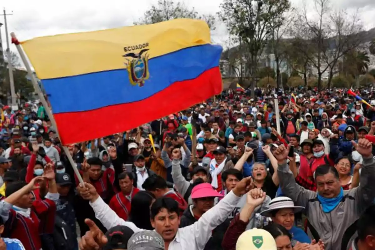 Crowd of people protesting with a large Ecuadorian flag waving at the front Crowd of people protesting with a large Ecuadorian flag waving at the front