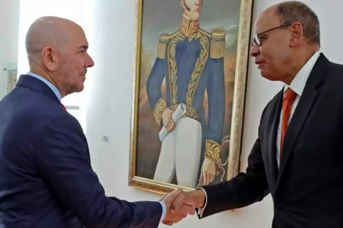 Two men in suits shake hands in front of a painting of a military officer in a blue and gold uniform.