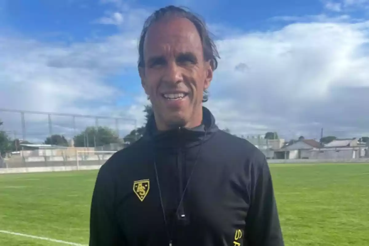 Hombre sonriente con chaqueta deportiva negra en un campo de fútbol al aire libre Hombre sonriente con chaqueta deportiva negra en un campo de fútbol al aire libre
