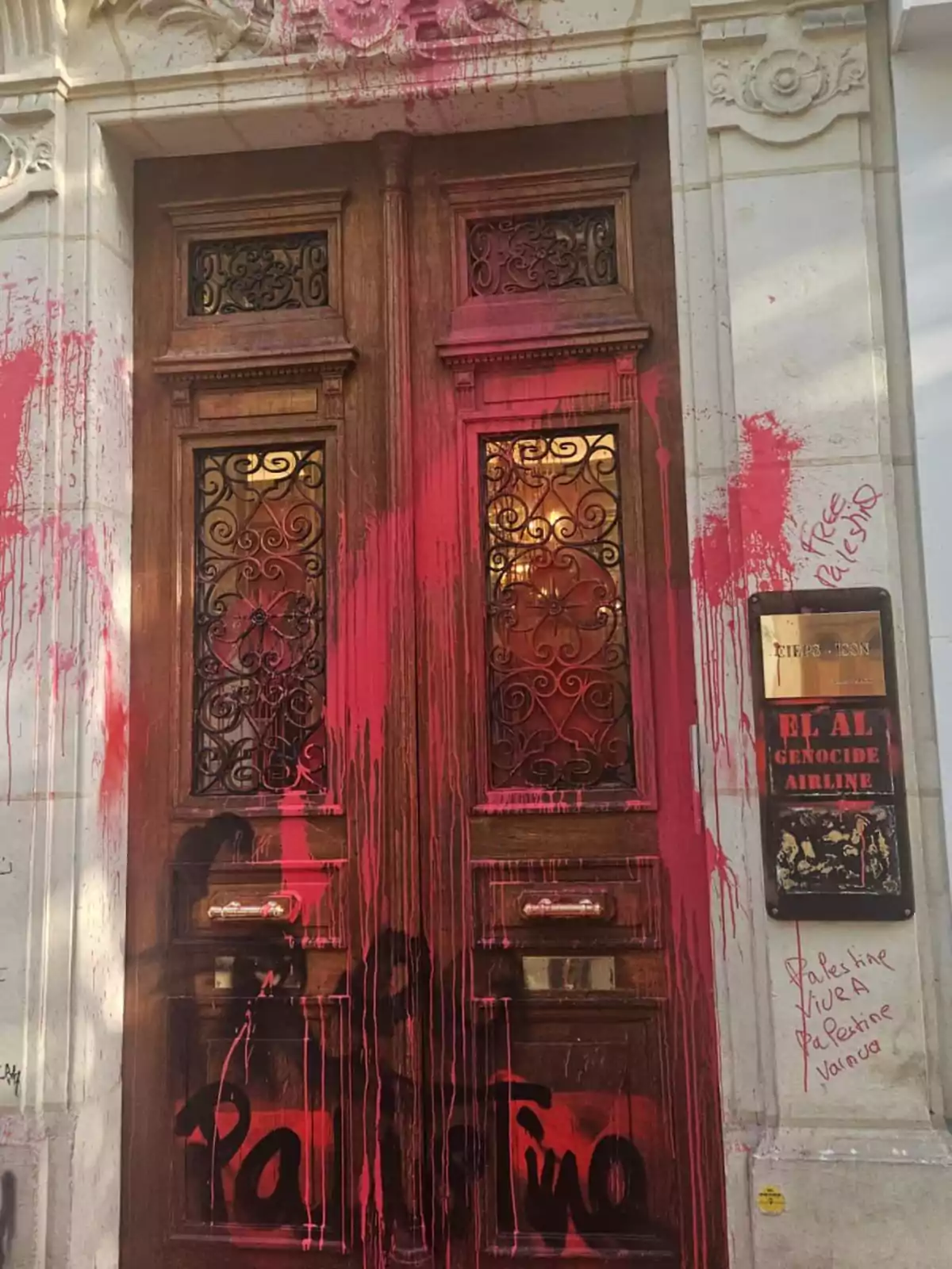 Puerta de madera antigua con vitrales y detalles de hierro, cubierta de pintura roja y grafitis relacionados con Palestina en la pared y la puerta Puerta de madera antigua con vitrales y detalles de hierro, cubierta de pintura roja y grafitis relacionados con Palestina en la pared y la puerta
