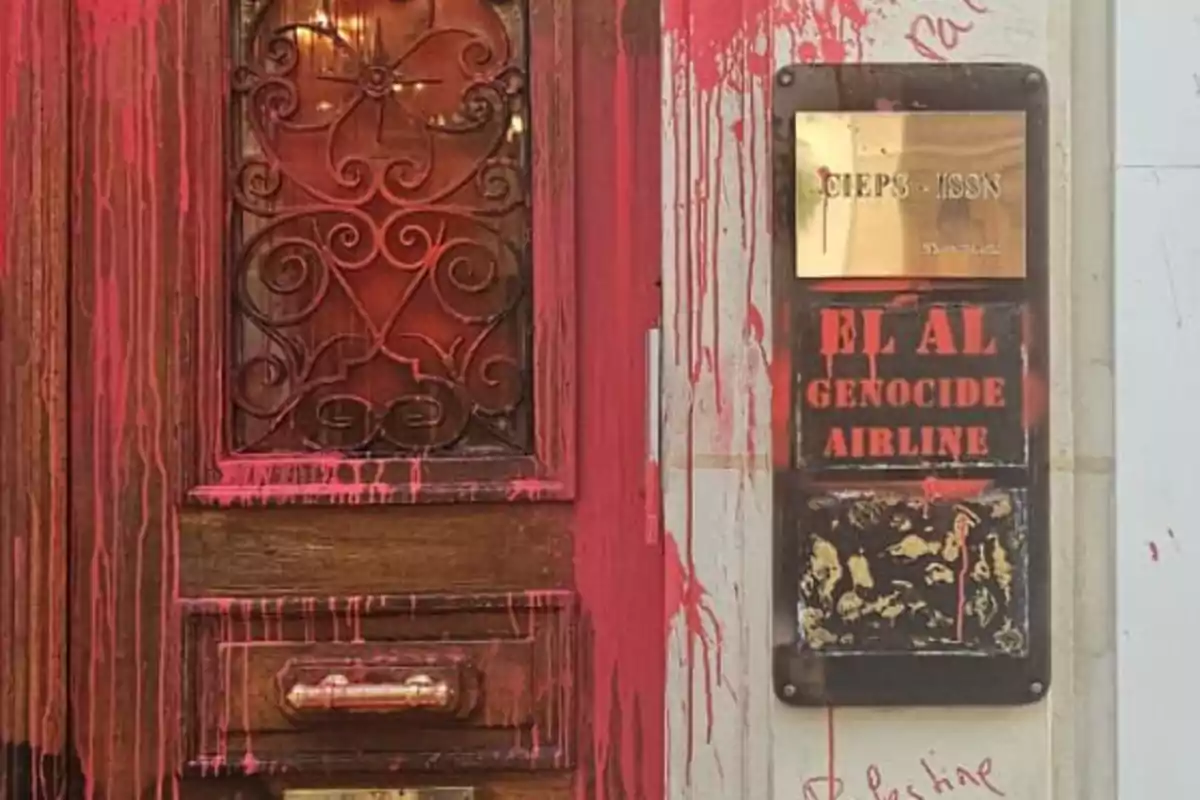 Puerta de madera y letrero manchados con pintura roja, con un mensaje de protesta escrito en el letrero