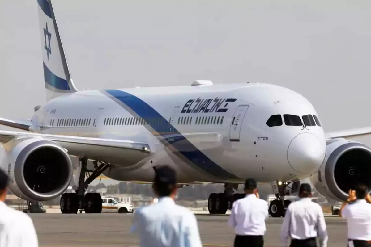 Avión de la aerolínea El Al en una pista de aterrizaje con varias personas uniformadas observando al frente Avión de la aerolínea El Al en una pista de aterrizaje con varias personas uniformadas observando al frente