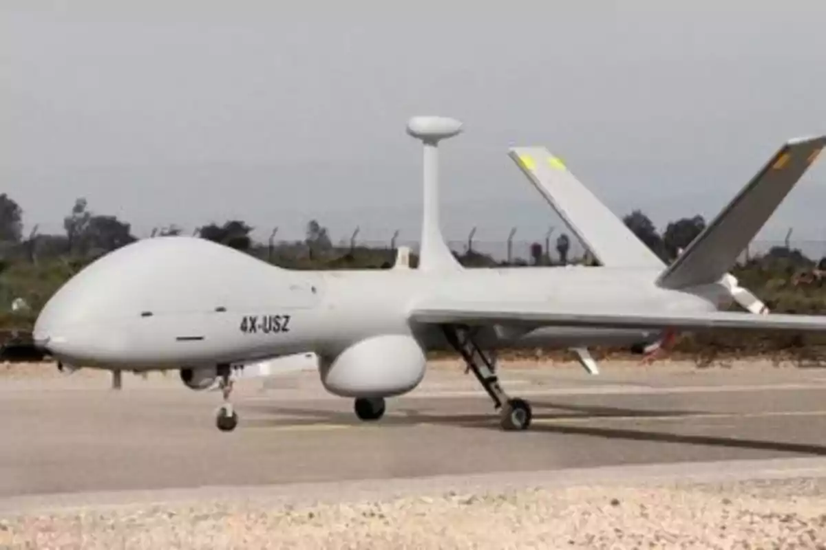 Dron militar gris estacionado en una pista de aterrizaje con vegetación al fondo