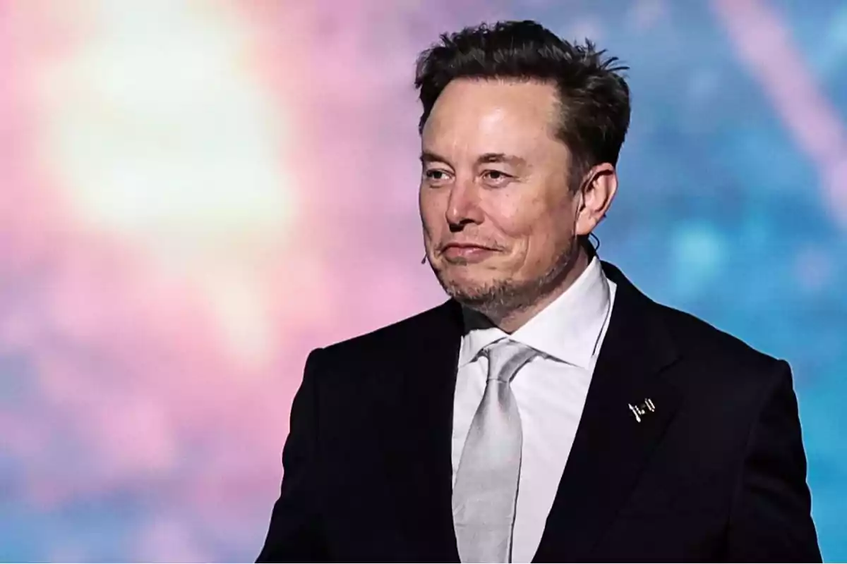 Man in a dark suit and light tie smiling in front of a colorful blurred background