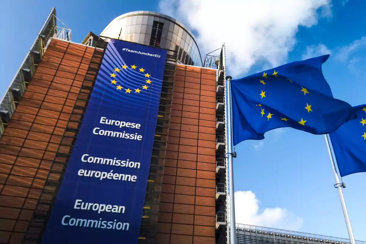 European Commission building with a European Union flag waving in front of a blue sky European Commission building with a European Union flag waving in front of a blue sky