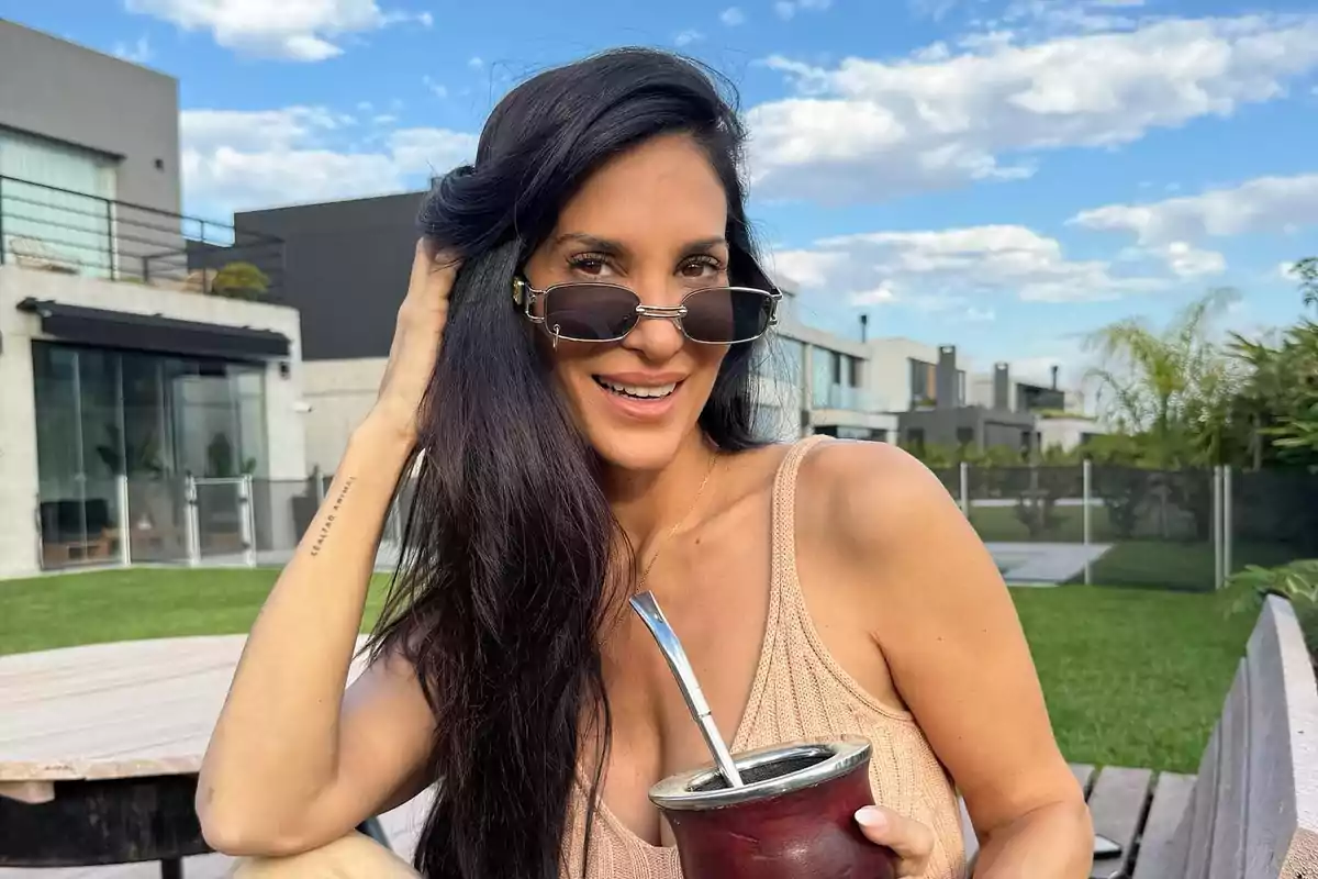 Mujer sonriente con gafas de sol sosteniendo un mate en un jardín moderno