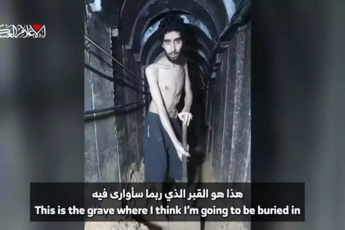Thin, jerseyless man inside a dark tunnel holding a shovel with a serious expression, accompanied by Arabic and English subtitles.