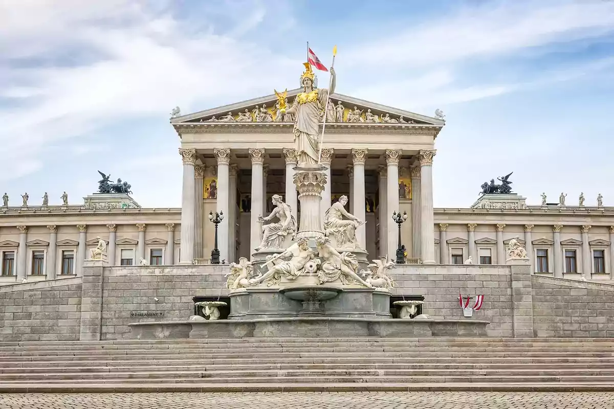 Facade of the Austrian Parliament building with a fountain and sculptures in the foreground under a partly cloudy sky Facade of the Austrian Parliament building with a fountain and sculptures in the foreground under a partly cloudy sky
