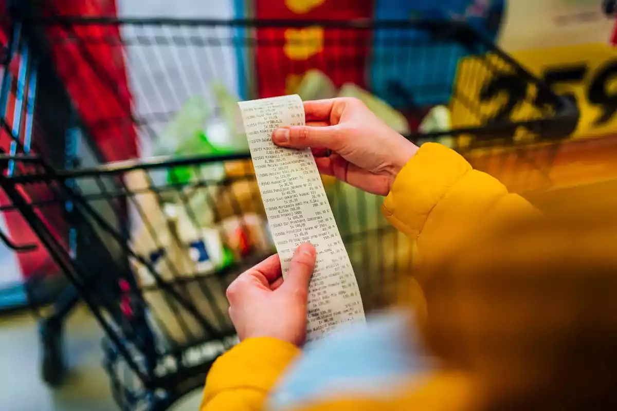 Person wearing a yellow jacket checking a receipt in front of a full shopping cart. Person wearing a yellow jacket checking a receipt in front of a full shopping cart.