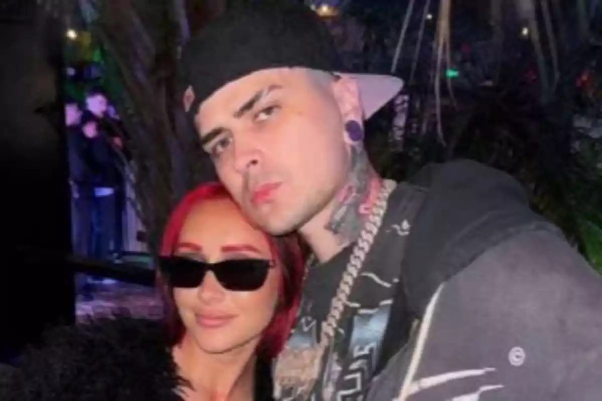 Two people pose together in a nighttime setting; one is wearing dark sunglasses and the other a black cap worn backwards. Two people pose together in a nighttime setting; one is wearing dark sunglasses and the other a black cap worn backwards.