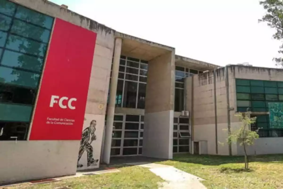 Modern building of the Faculty of Communication Sciences with a large red sign and glass windows, surrounded by grass and small trees. Modern building of the Faculty of Communication Sciences with a large red sign and glass windows, surrounded by grass and small trees.