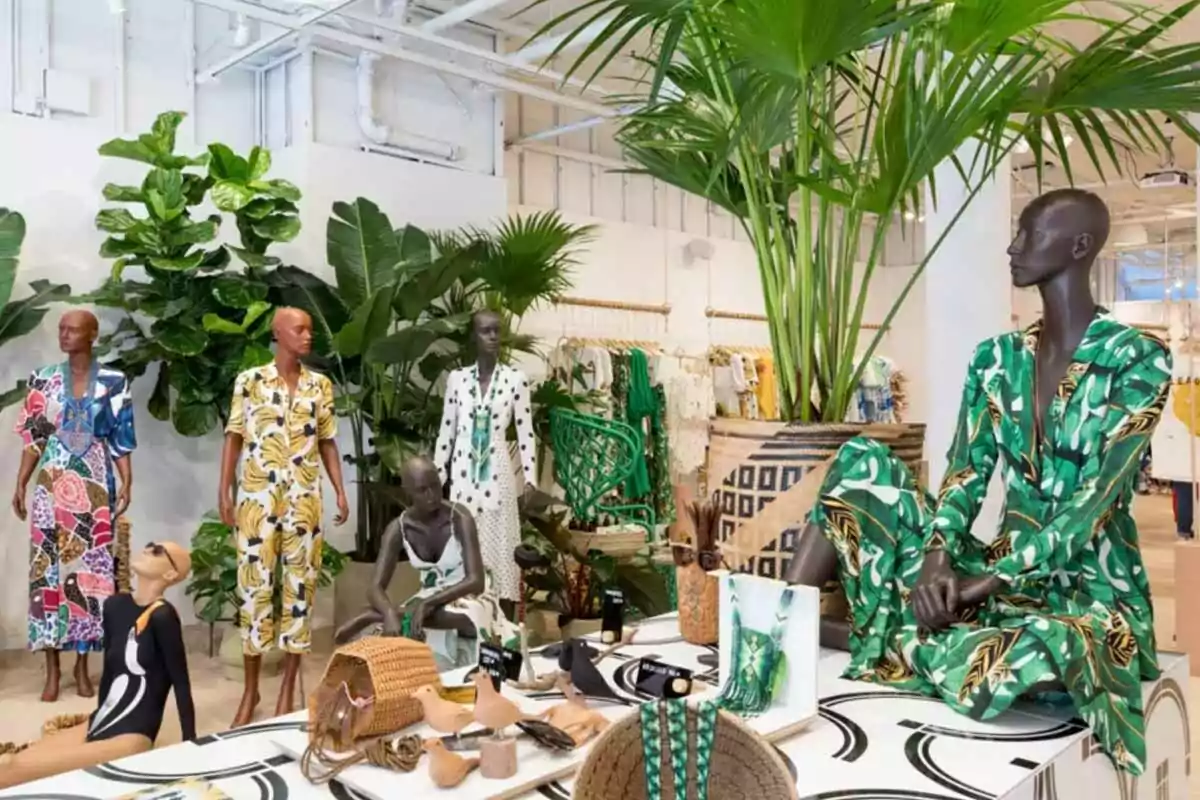 Maniquíes con ropa colorida y estampados tropicales en una tienda decorada con plantas grandes y accesorios de moda sobre una mesa