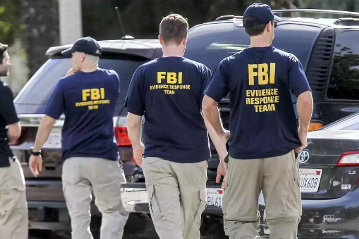 Agentes del FBI con camisetas azules y pantalones beige caminan junto a vehículos estacionados