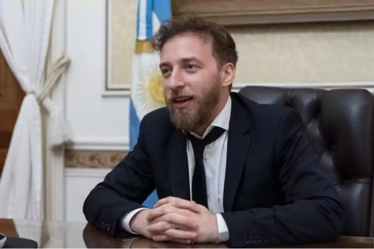 Bearded man in a dark suit sitting at a desk with an Argentine flag in the background Bearded man in a dark suit sitting at a desk with an Argentine flag in the background