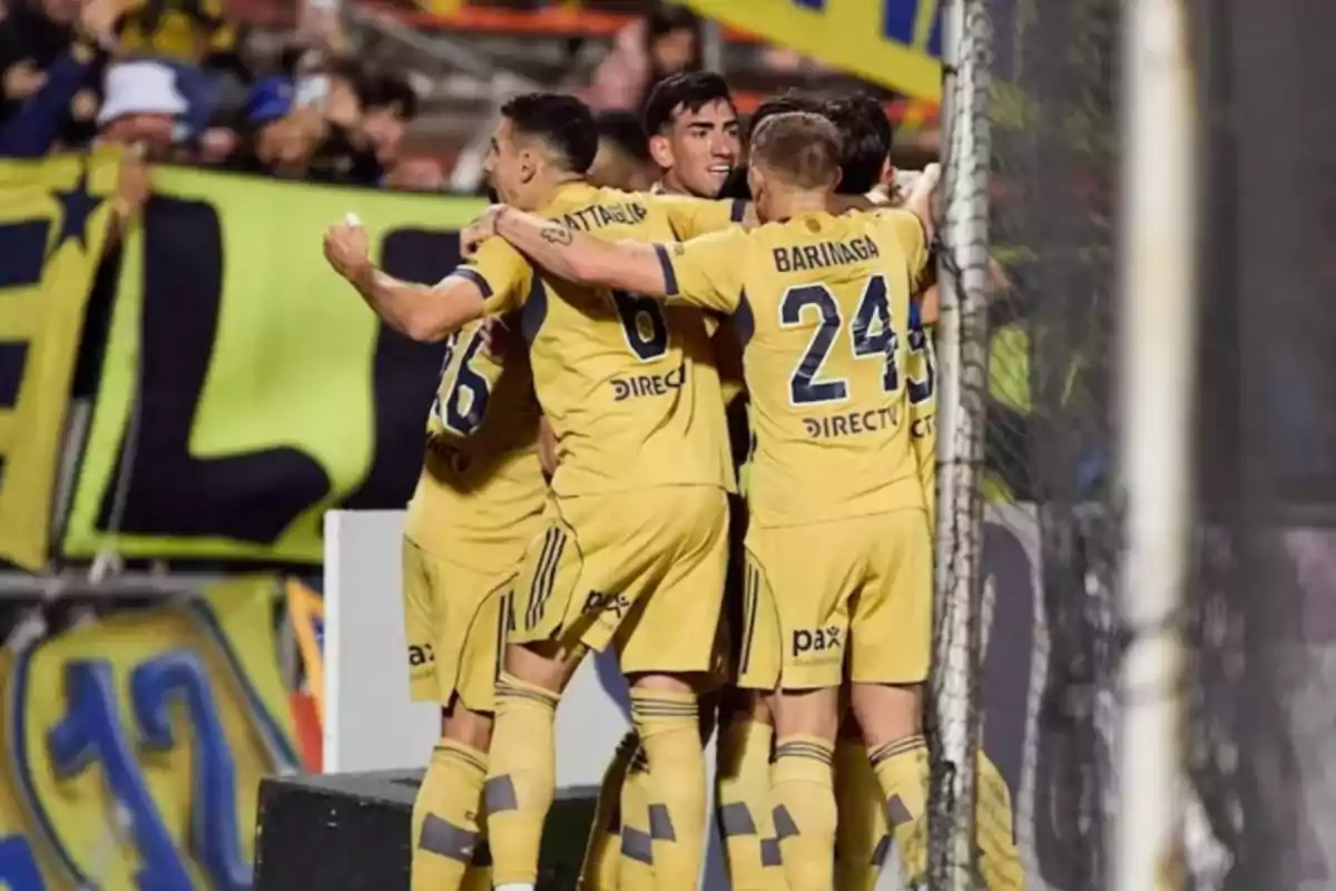 Soccer players in yellow uniforms celebrate a goal hugging near the goal while fans watch from the stands.