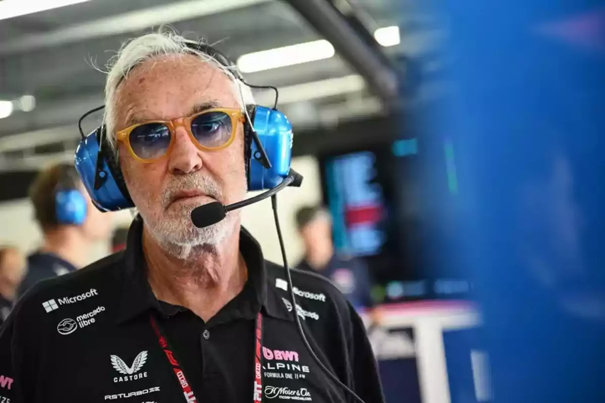 Hombre mayor con gafas de sol y auriculares azules con micrófono en un ambiente de equipo de automovilismo Hombre mayor con gafas de sol y auriculares azules con micrófono en un ambiente de equipo de automovilismo