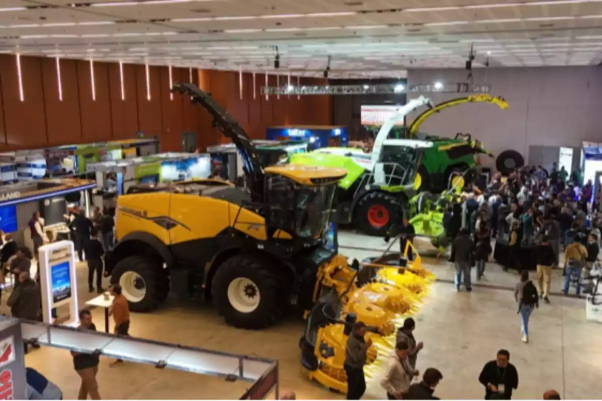 Exhibition of agricultural machinery with several large harvesters and many people walking around the booths at an indoor event Exhibition of agricultural machinery with several large harvesters and many people walking around the booths at an indoor event