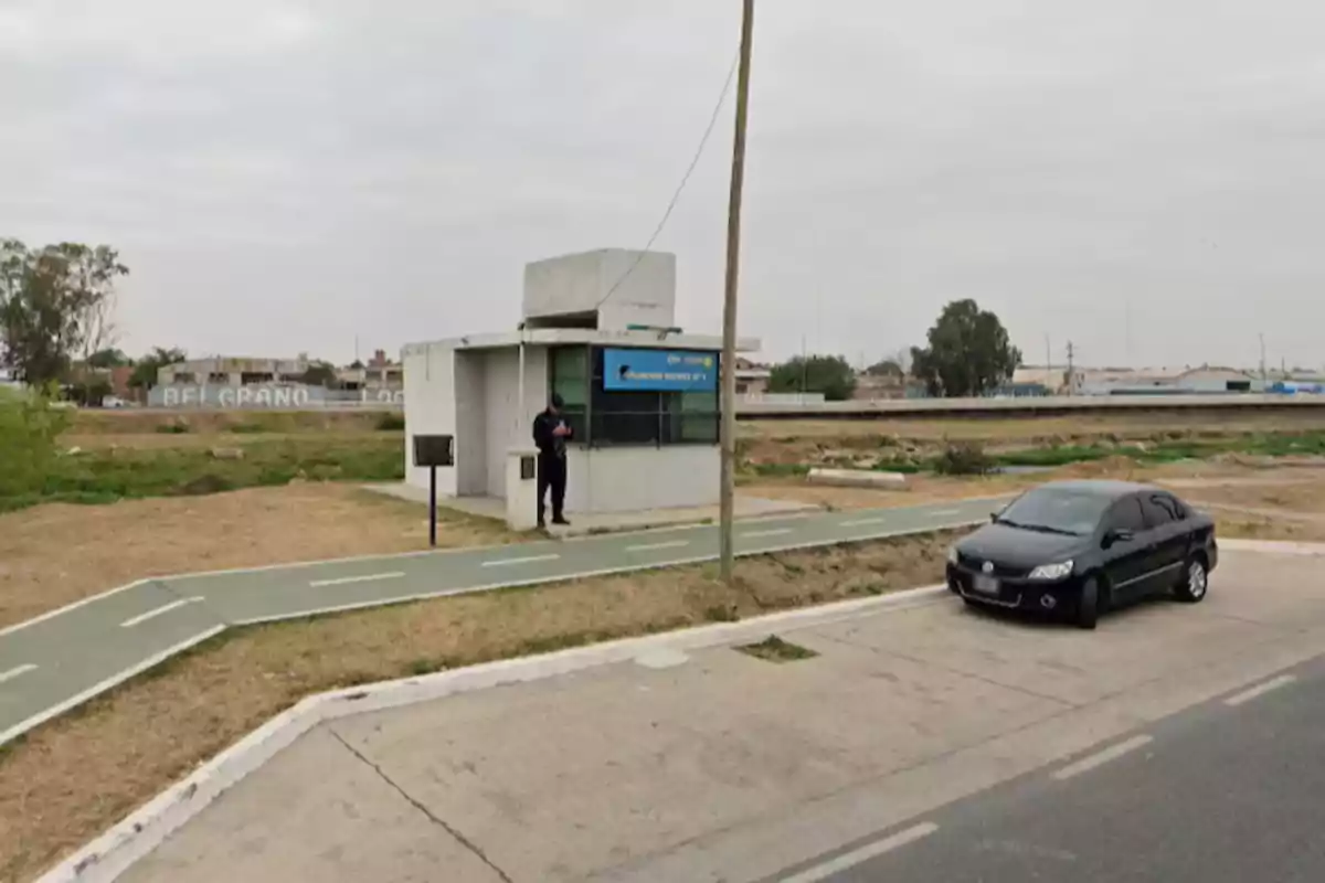 A police officer is standing next to a small guard booth near a bike lane and a black car parked on the street on a cloudy day. A police officer is standing next to a small guard booth near a bike lane and a black car parked on the street on a cloudy day.