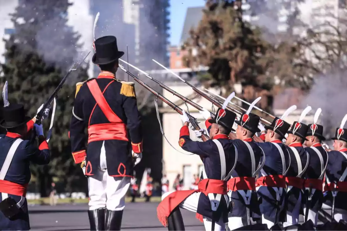 Soldados con uniformes históricos azules, blancos y rojos realizan una salva de fusil en formación durante una ceremonia al aire libre Soldados con uniformes históricos azules, blancos y rojos realizan una salva de fusil en formación durante una ceremonia al aire libre