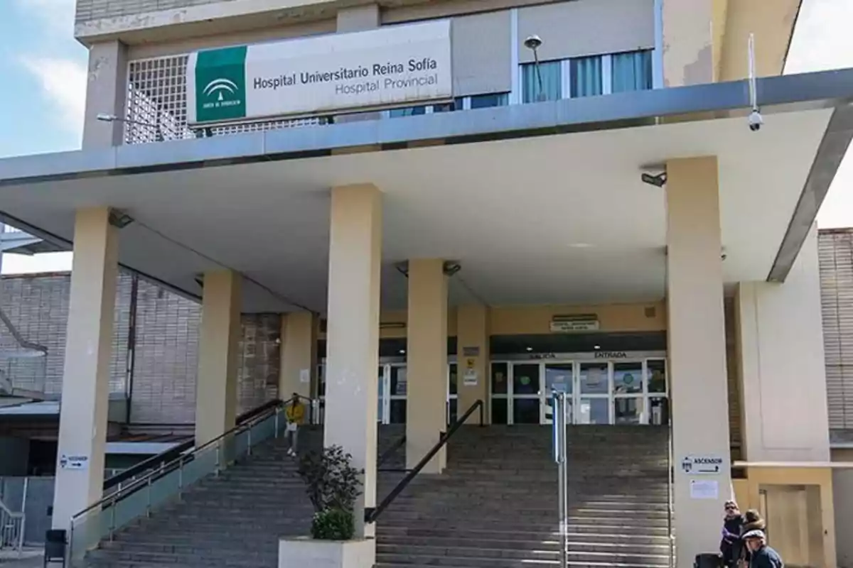 Main facade of the Reina Sofía University Hospital with access stairs and several people at the entrance Main facade of the Reina Sofía University Hospital with access stairs and several people at the entrance