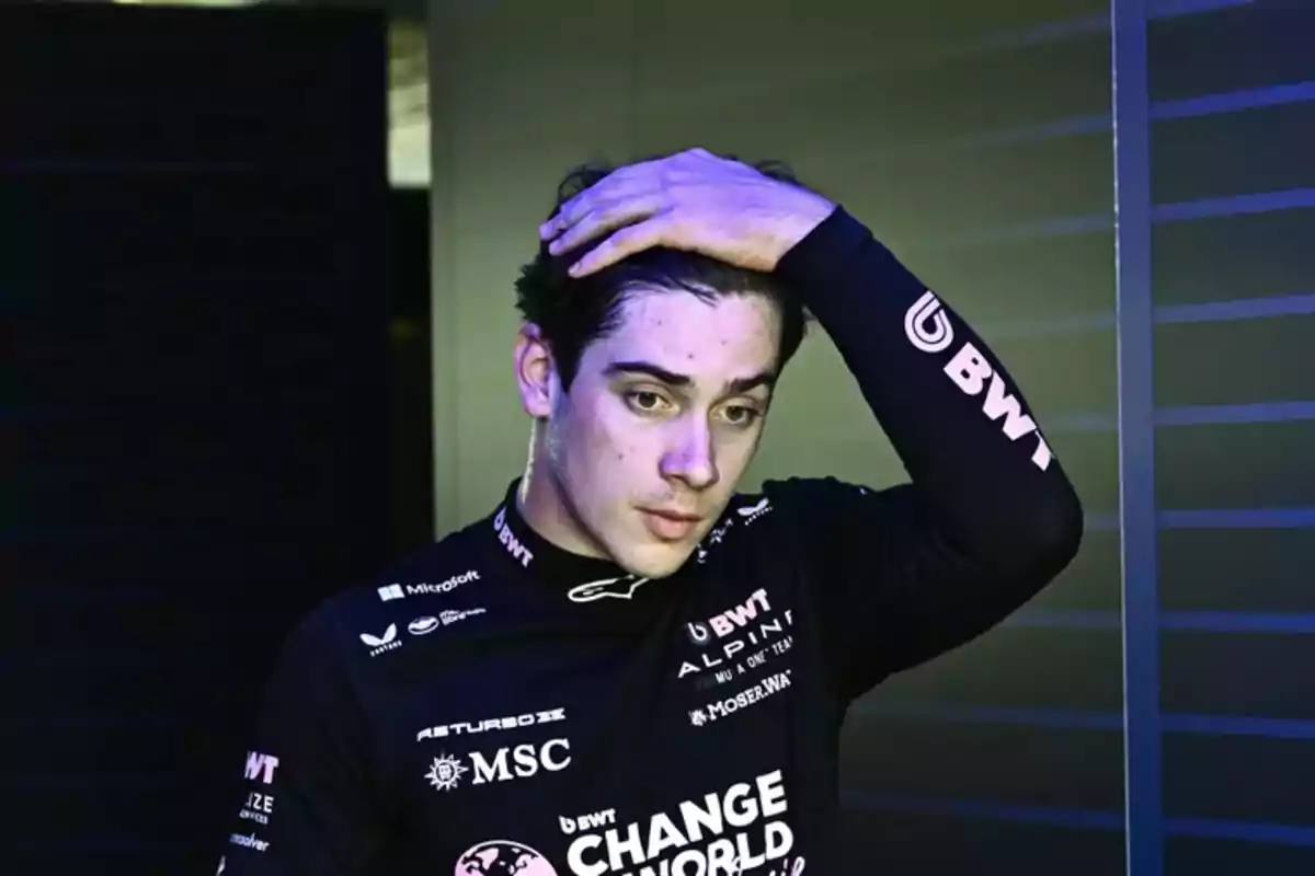 Young race car driver with a serious expression and hand on his head, wearing a black uniform with sponsor logos