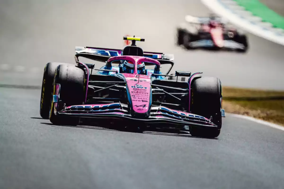 Pink and blue Formula 1 car driving on a racetrack with another car blurred in the background
