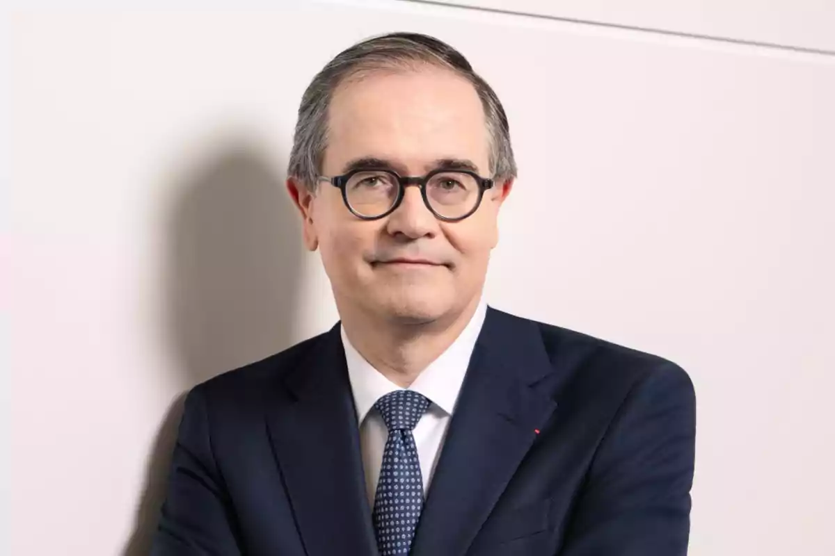 Hombre de mediana edad con gafas y traje azul posando frente a una pared clara Hombre de mediana edad con gafas y traje azul posando frente a una pared clara