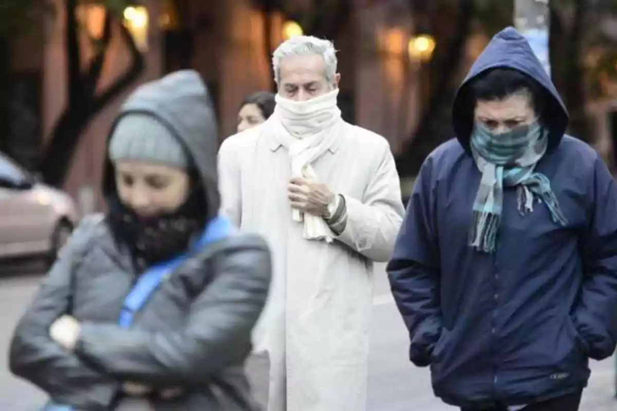 People walking down the street bundled up in scarves, hats, and jackets on a cold day