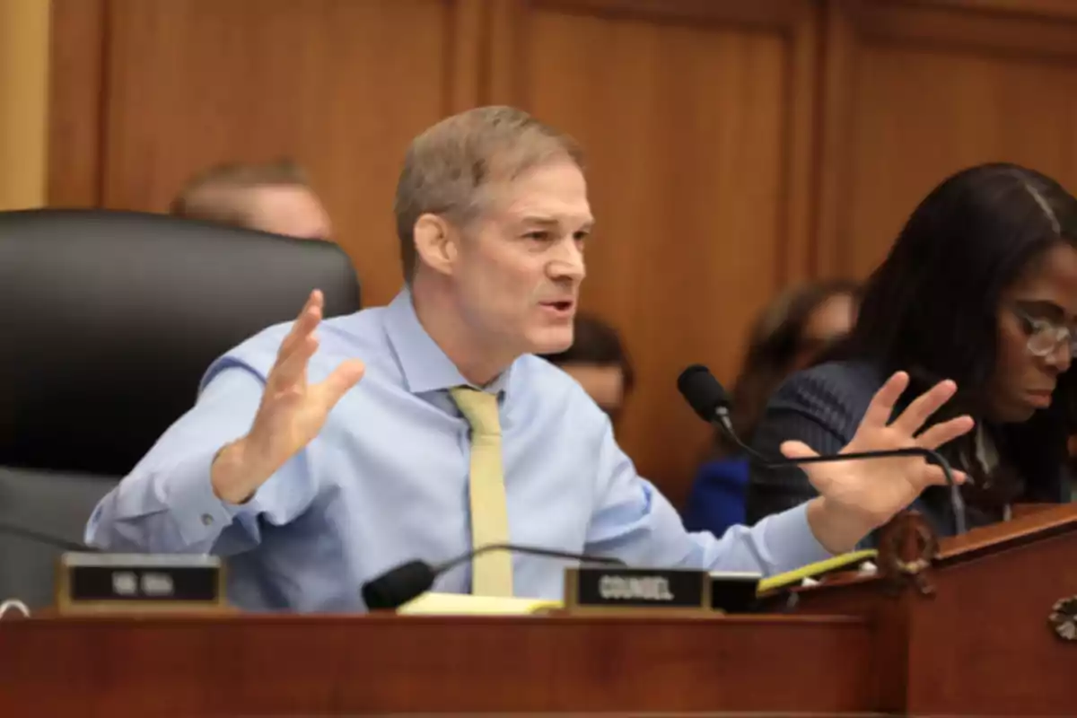 Light-haired man in a blue jersey and yellow tie gesturing while speaking at a formal meeting next to a woman with glasses Light-haired man in a blue jersey and yellow tie gesturing while speaking at a formal meeting next to a woman with glasses