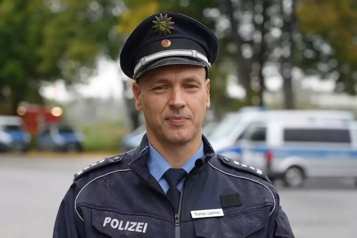German police officer in uniform standing outdoors with blurred police vehicles in the background German police officer in uniform standing outdoors with blurred police vehicles in the background
