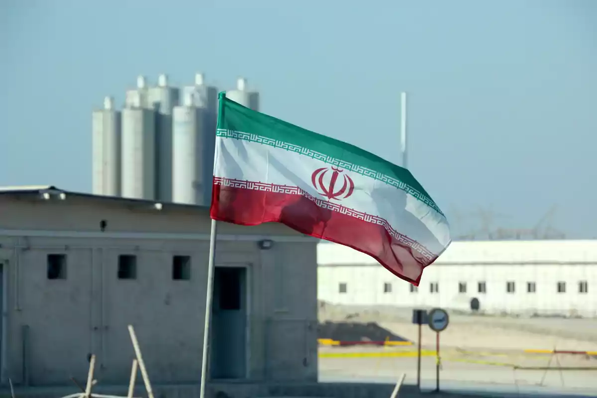 Bandera de Irán ondeando frente a edificios industriales bajo un cielo despejado Bandera de Irán ondeando frente a edificios industriales bajo un cielo despejado