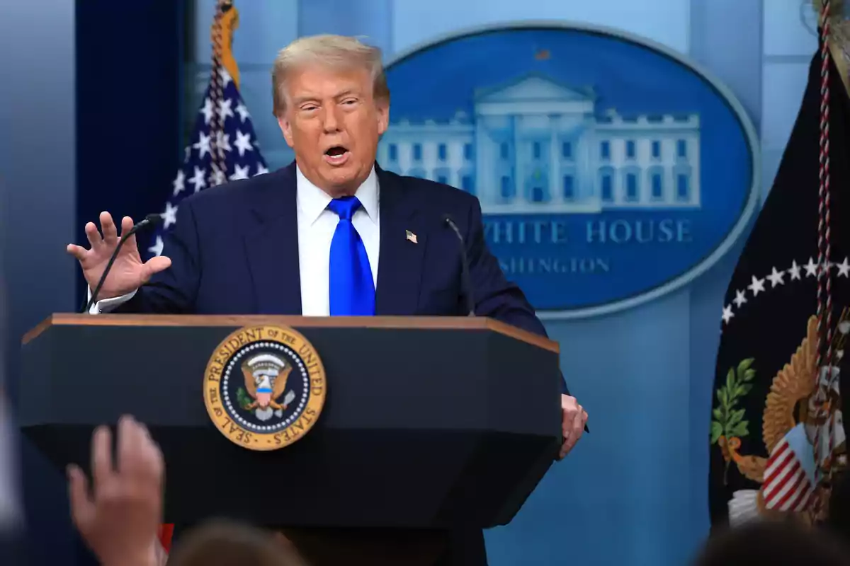 Un hombre de traje azul y corbata azul habla en un podio presidencial frente a un fondo con el logo de la Casa Blanca y banderas de Estados Unidos