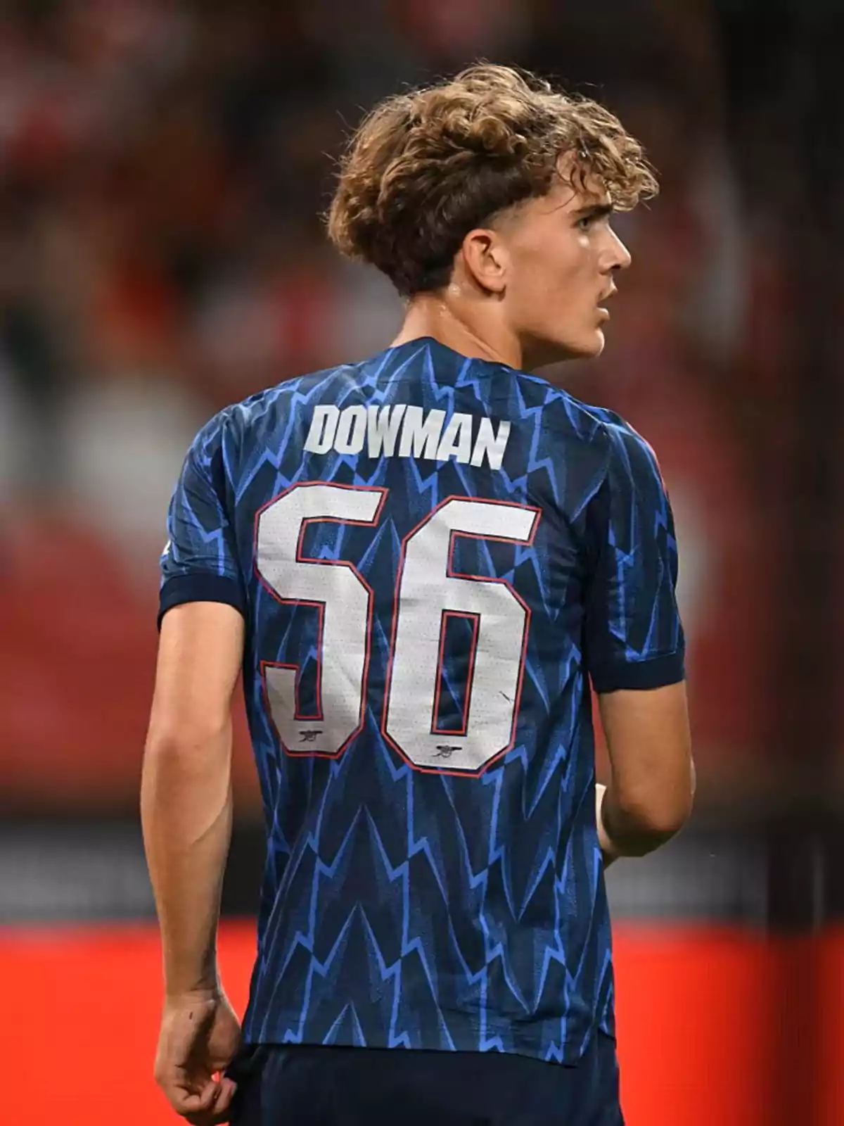 Joven futbolista con cabello rizado usando un uniforme azul con el nombre Dowman y el número 56 en la espalda durante un partido