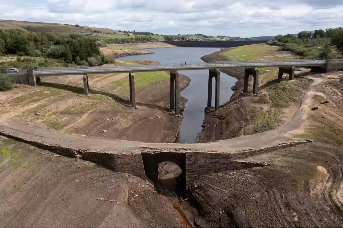 Puente moderno sobre un embalse con bajo nivel de agua y un antiguo puente de piedra parcialmente expuesto en primer plano rodeado de tierra seca y vegetación escasa Puente moderno sobre un embalse con bajo nivel de agua y un antiguo puente de piedra parcialmente expuesto en primer plano rodeado de tierra seca y vegetación escasa