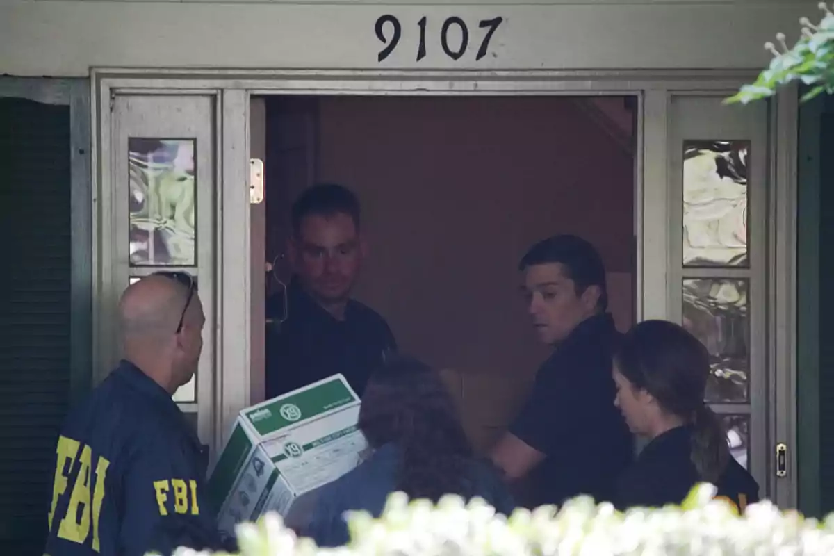 Agentes del FBI entrando a una casa con el número 9107 mientras cargan cajas de evidencia Agentes del FBI entrando a una casa con el número 9107 mientras cargan cajas de evidencia