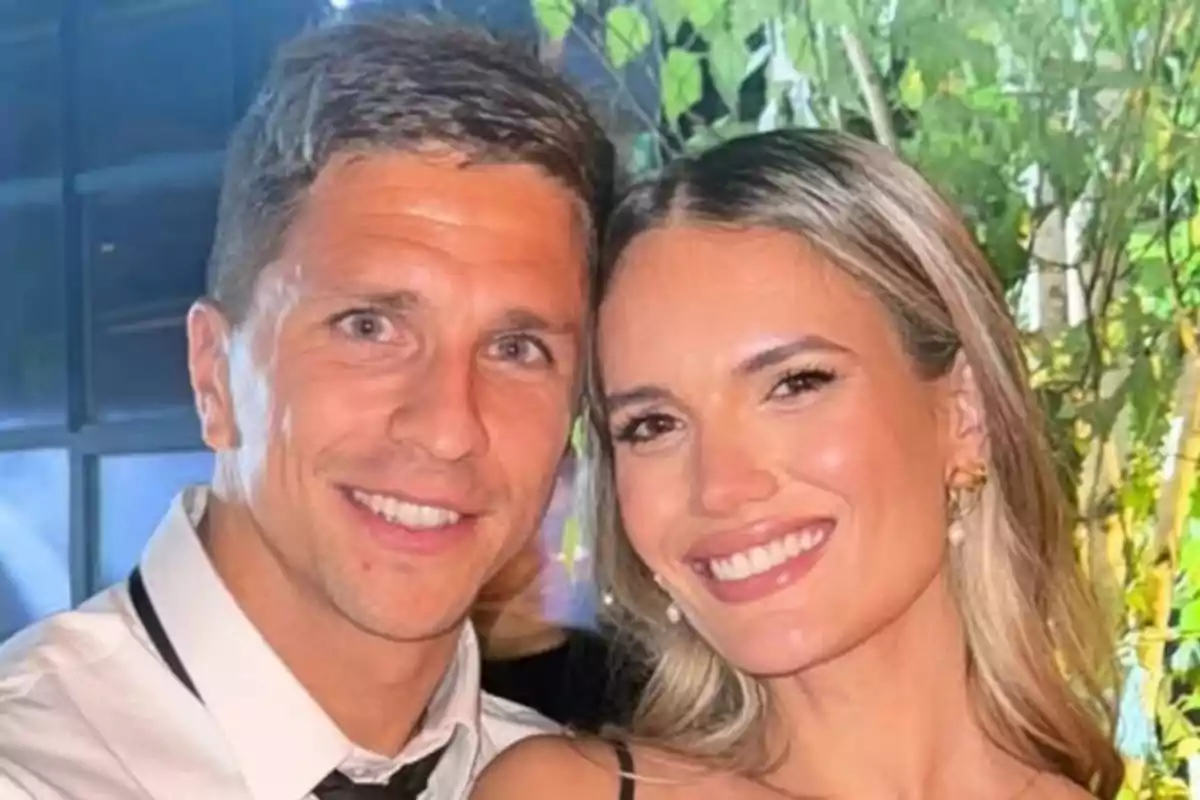 Couple smiling and posing together in a well-lit setting with plants in the background Couple smiling and posing together in a well-lit setting with plants in the background